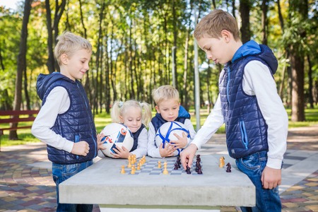 The topic children learning, logical development, mind and math, miscalculation moves advance. large family brothers and sister Caucasian boys and girl playing chess park bright sunny weather autumn.の写真素材