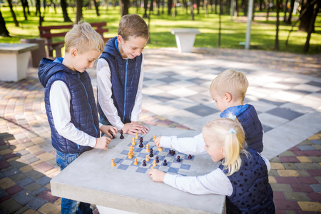 The topic children learning, logical development, mind and math, miscalculation moves advance. large family brothers and sister Caucasian boys and girl playing chess park bright sunny weather autumn.の写真素材