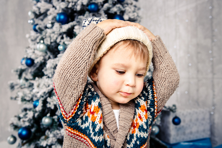 Christmas theme and children. Little Caucasian boy child in a warm hat and sweater posing, eating sweetness, dirty face. Christmas morning. New Years holidays.の写真素材
