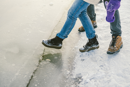 Trying the danger of the foot, testing the thin ice near the shore. A pair of lovers walk with a walk along a frozen lake to press foot on the ice.の写真素材