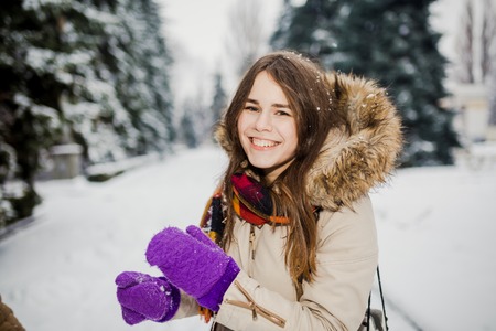 Beautiful young Caucasian woman joy happiness smile play with snow near a coniferous tree in a snowy park.の写真素材