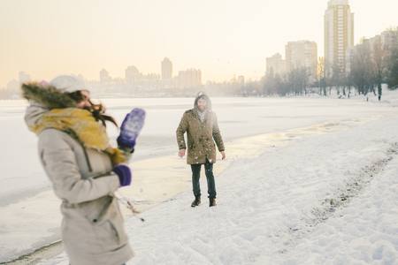 Young Caucasian people in love heterosexual couple have a date in winter near a frozen lake. Active holiday holiday Valentine's Day, playing snowballs and playing joy.の写真素材