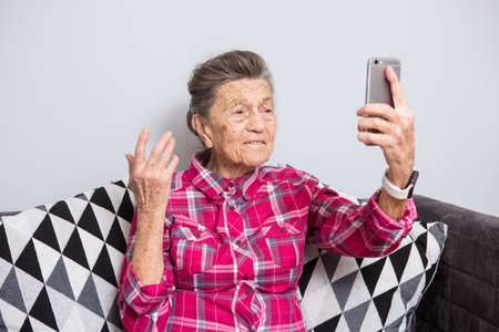 A very old senior Caucasian grandmother with gray hair and deep wrinkles sits home on couch in jeans...