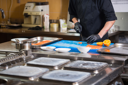 Theme cooking is a profession of cooking. Close-up of a Caucasian man's hand in a restaurant kitchen preparing red fish fillets salmon meat in black latex gloves uniform.の写真素材