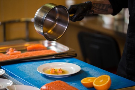 Theme cooking is a profession of cooking. Close-up of a Caucasian man's hand in a restaurant kitchen preparing red fish fillets salmon meat in black latex gloves uniform.の写真素材