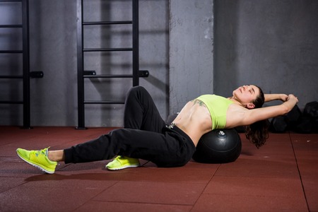 Theme sport and health. A strong muscular Caucasian woman in the gym lies with her back on a padded black kneading ball, warming up her back muscles. Massage spine equipping. Back pain relief.の写真素材