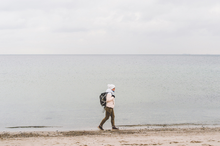 One caucasian man young caucasian woman tourist with a black backpack on a sandy beach near the Baltic sea in winter. Theme trip alone. Thoughts and dreams overlooking the horizon.の写真素材