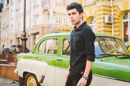 Portrait of a model young handsome sexy male brunette guy with dark skin Turkish Middle Eastern brunette posing smoking a cigarette near old retro car on the street.の写真素材
