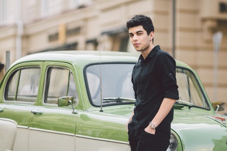 portrait, handsome, male, model, brunette Mediterranean race Turkish man stands near a retro car of green color posing in a black shirt and jeans in the city.の写真素材
