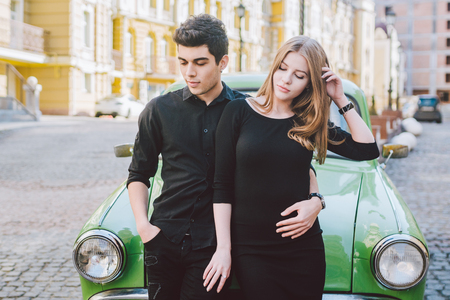 Young multiracial couple, male and female lovers heterosexual people students. Beautiful models posing standing near a retro car in the city. Dressed in black clothes.の写真素材
