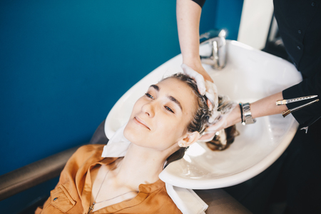 beauty and people concept. Hairdresser washing hair of happy young woman, girl and do relaxing massage at beauty saloon.の写真素材