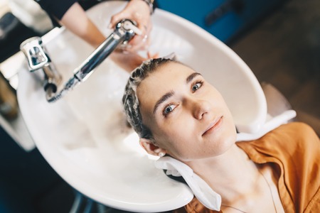 beauty and people concept. Hairdresser washing hair of happy young woman, girl and do relaxing massage at beauty saloon.の写真素材