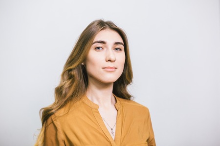 Portrait of a beautiful young woman with long curly hair on a plain white background. The theme is beauty and fashion. Caucasian student girl posing after a haircut and styling in a beauty salonの写真素材