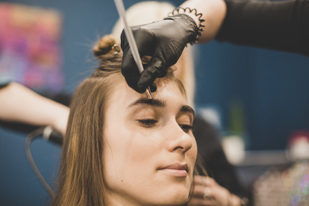 Professional Make Up Artist Doing Make Up In Beauty Salon. Eyebrow dyeing. master paints eyebrows with henna to beautiful girl, paints with brush in salon beautician makeup artist. Brow architecture.の写真素材