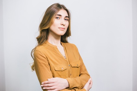 Portrait of a beautiful young woman with long curly hair on a plain white background. The theme is beauty and fashion. Caucasian student girl posing after a haircut and styling in a beauty salonの写真素材