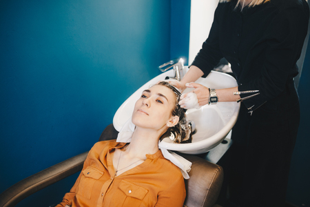 beauty and people concept. Hairdresser washing hair of happy young woman, girl and do relaxing massage at beauty saloon.の写真素材