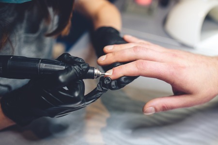Men's manicure. Professional manicure for man by manicure machine. A man receiving a manicure in the beauty salon. Beautician master trimming and removes cuticles.の写真素材