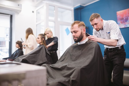 Close up shot of a man getting a trendy haircut at a hair salon. Male caucasian hairdresser serving...