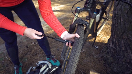Young caucasian woman athlete tourist cyclist uses a hand tool, a bicycle pump to inflate air into a...