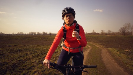 Athletic Caucasian woman eats protein bar ride on mountain bike on nature. Young sporty woman athlete in helmet resting while biting nutritional bar. Fitness woman eating energy snack outdoor.の写真素材