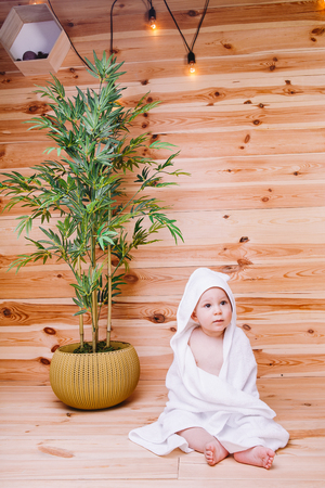 the baby wrapped in a white towel with ears sitting on wooden background near a bamboo tree in potの写真素材