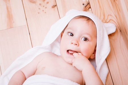 baby boy with brown eyes is five months old wrapped in a white towel with ears on wooden background brown.の写真素材
