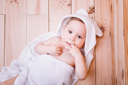baby boy with brown eyes is five months old wrapped in a white towel with ears on wooden background brown.の写真素材