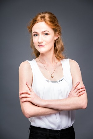 portrait of a young red-haired beautiful girl in the studio on a gray isolated background.の写真素材