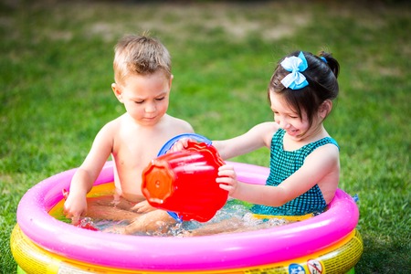 Subject childhood summer games in the yard. Caucasian brother and sister playing plastic toys bucket sitting in the waterの写真素材