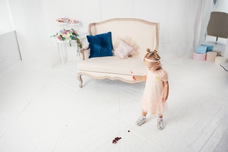 Little funny caucasian child girl dropped on the floor sweetness dessert cake and mess. Kindergarten and birthday party spoiled, fell sweet food on the floor at home.の写真素材