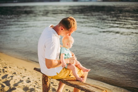 father and little son. Young caucasian dad sits on wooden bench overlooking the town Kiev and...