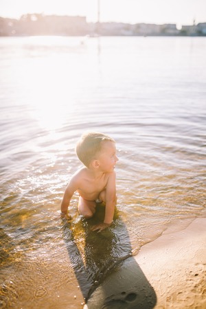 Theme is summer time and rest near the water. Little joyful Caucasian funny boy plays and enjoys in the river. The child is resting and swimming in the lake pond sandy beach.の写真素材