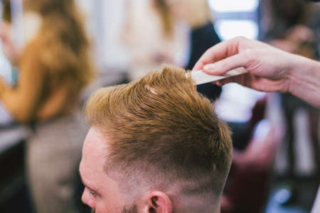 Barber Making Haircut Bearded Man In Barbershop. Professional stylist cutting client hair in salon. Barber using scissors and comb. Skillful hairdresser cutting male hair. Hair Care Service Concept.の写真素材