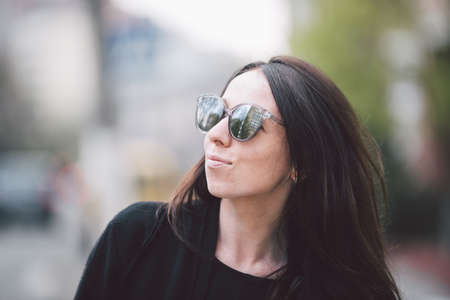 Portrait of a young beautiful caucasian woman on the background of the street. Model girl with long hair and sunglasses with reflection posing in black clothes in an urban environment.の写真素材