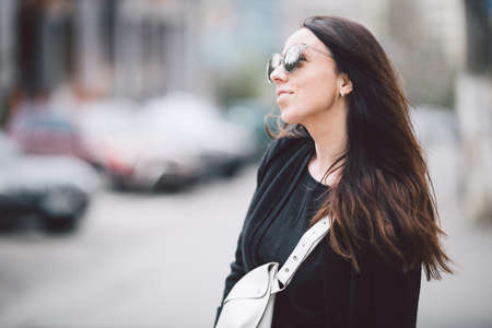 Portrait of a young beautiful caucasian woman on the background of the street. Model girl with long hair and sunglasses with reflection posing in black clothes in an urban environment.の写真素材
