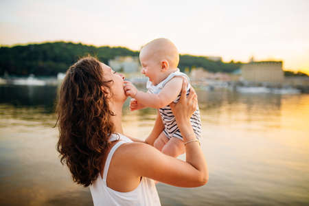 Happy family on the beach. Son child mother boy and baby hugging on beach near river or lake. Happy family on the beach. Mom and son hugging at sunset.の写真素材