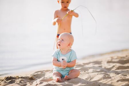 Smiling baby boy sitting on the sand near river. Summer concept. Holiday relaxing, beach vacation. Funny cute child making vacations and enjoying summer. Spring holidays, summer vacation.の写真素材