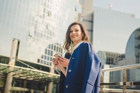 Office buildings city people in suit. Caucasian businesswoman using smartphone with hand. Business concept. Portrait stylish business woman in fashionable clothes holding Phone near office building.の写真素材