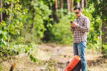 Hipster young man with backpack using smart phone on beautiful nature.Travel concept. Outdoor travel. Travel and explore. Backpacker male Going in forest Gps Route. Portrait hiker using mobile phone.の写真素材