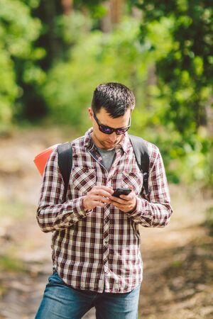 Hipster young man with backpack using smart phone on beautiful nature.Travel concept. Outdoor travel. Travel and explore. Backpacker male Going in forest Gps Route. Portrait hiker using mobile phone.の写真素材