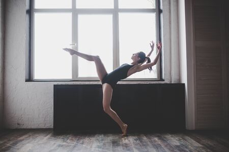 Plasticity slim woman dancing near window. Professional dancer enjoy dance. Lady Dancer Training Modern Ballet In Class. Contemporary dance performer. Daylight, silhouette beautiful body. Dance theme.の写真素材
