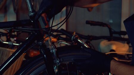theme small business bike repair. Young brunette Caucasian man in protective glasses, gloves and fartuhe uses hand tools to repair and tuning Rim Brakes and wheel spinning bike in a garage workshop.の写真素材