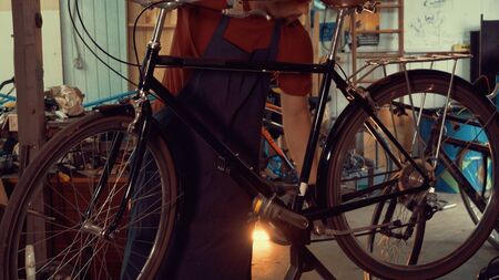 theme small business bike repair. A young Caucasian brunette man wearing safety glasses, gloves and an apron insists the speed switches on the bicycle handlebar in the garage of the workshop.の写真素材