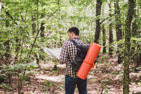 Man with Backpack and map searching directions in wilderness area. Tourist with backpack using map...