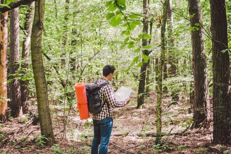 Man with Backpack and map searching directions in wilderness area. Tourist with backpack using map...
