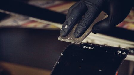 Ski maintenence. Removing excess wax from race ski base plastic scraper. Ski service and repair. Winter shop worker doing base repair. Rental workshop service. Repairman In Workshop Ski Service.の写真素材