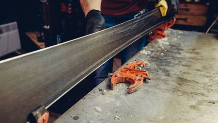 Male worker of ski service workshop doing sharpening and repair of skis. Sharpening ski edges with a manual side-edge tuning tool fitted with a diamond stone. Theme repair of ski curb.の写真素材