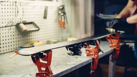 Male worker of ski service workshop doing sharpening and repair of skis. Sharpening ski edges with a manual side-edge tuning tool fitted with a diamond stone. Theme repair of ski curb.の写真素材