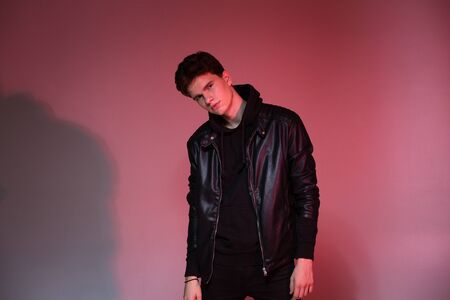 Cute brutal man in black leather jacket model style. Portrait of a handsome guy on pink studio...