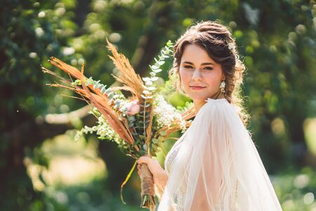 Beautiful bride with bouquet flowers stands on forest background. Rustic style. beautiful bride in...